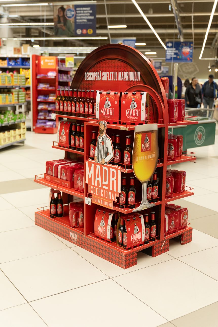Stand promoțional Madri Excepcional într-un supermarket, decorat în roșu intens și cu sticle de bere în ambalaj multipack.