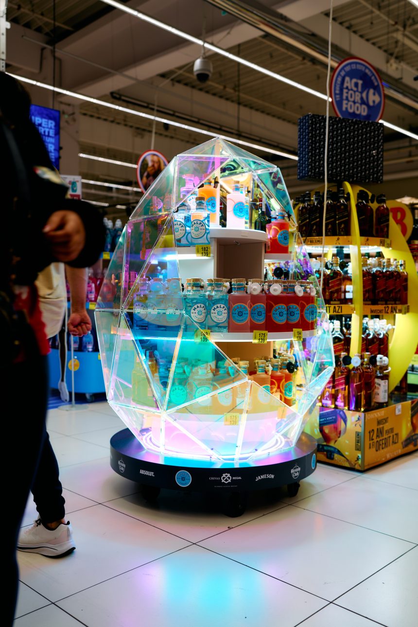 Stand promoțional în formă de ou luminos cu sticle de apă tonică și mixer Lala Tequila, într-un supermarket Carrefour, decorat cu lumini LED colorate.